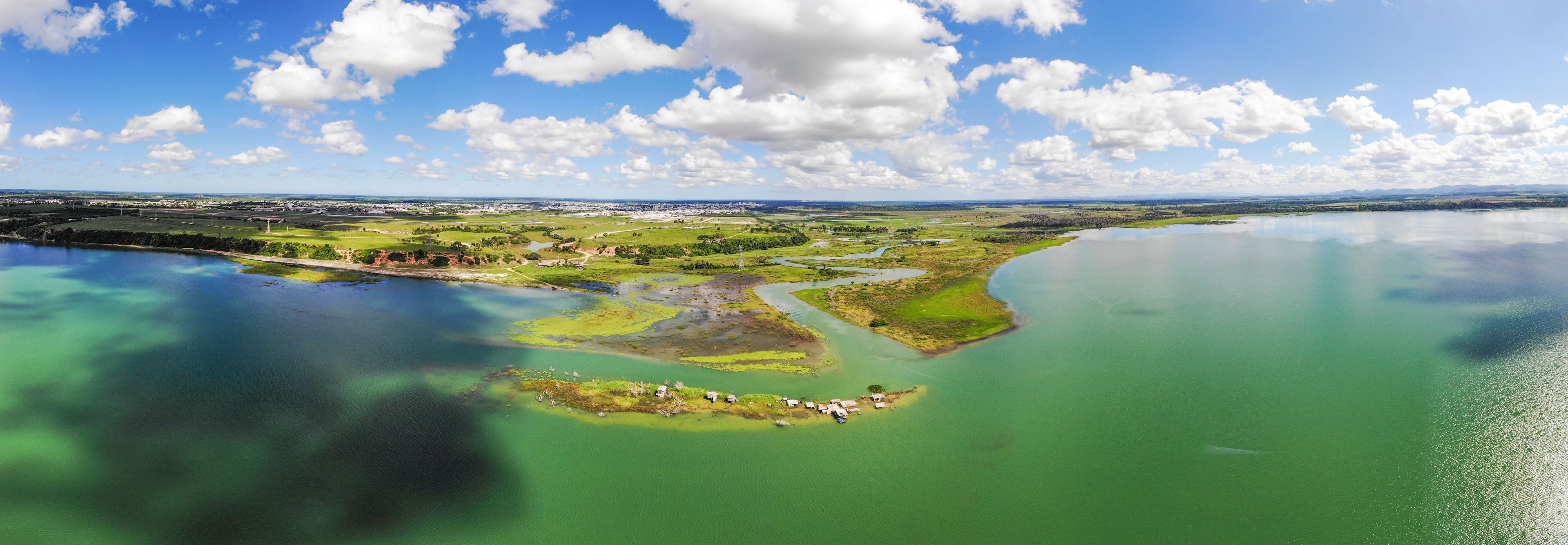 Una extensa masa de agua de color verdoso, rodeada de campos verdes y algunos edificios pequeños.