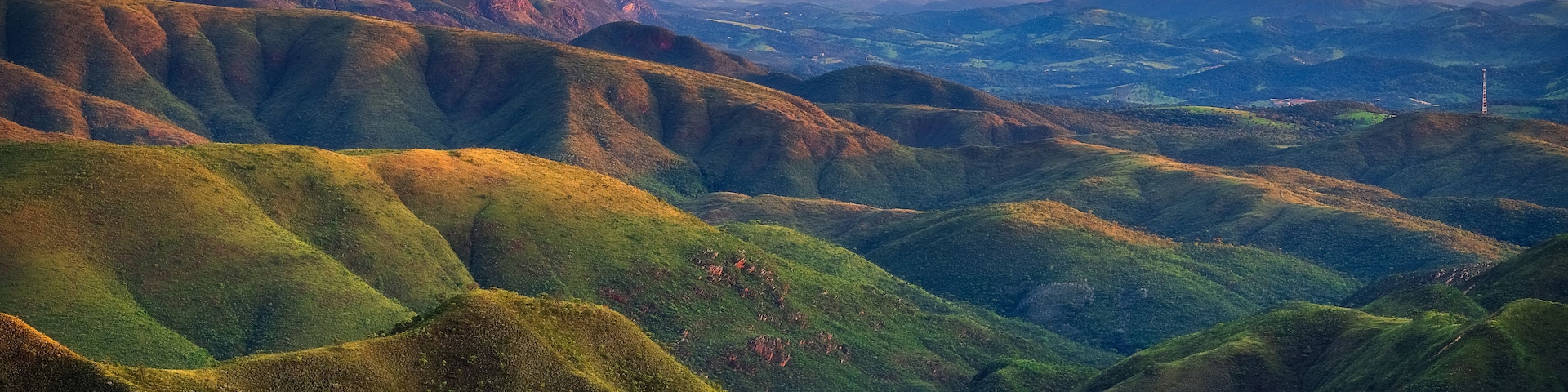 Rolling hills with lush greenery and distant mountains under a clear sky.