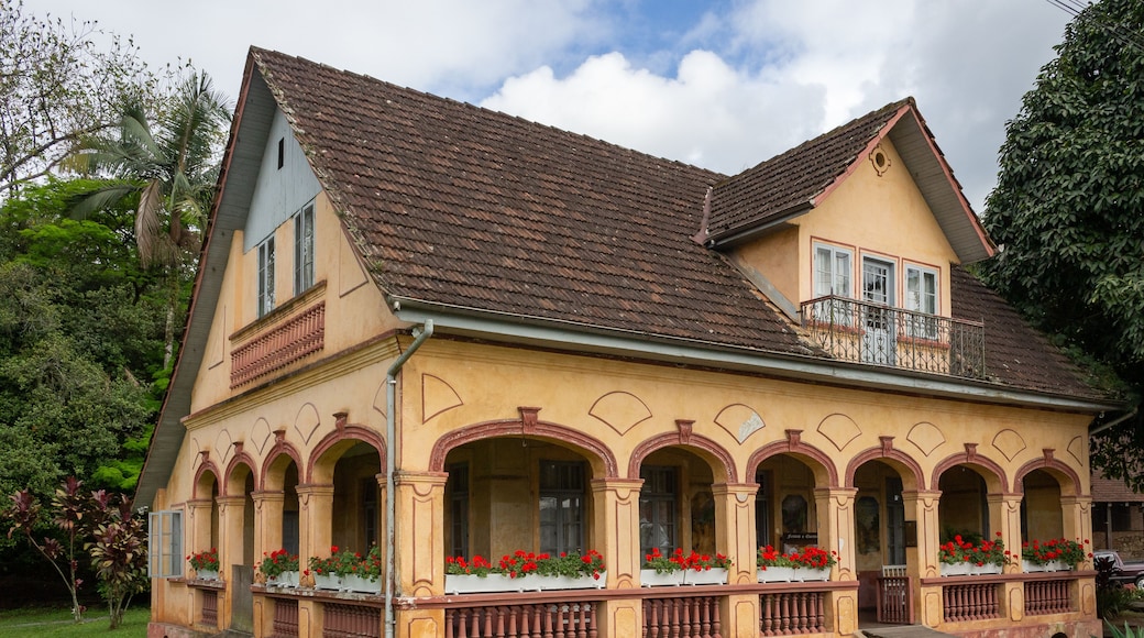 A two-story house with a brown tiled roof, arched windows, and a balcony with red flowers.