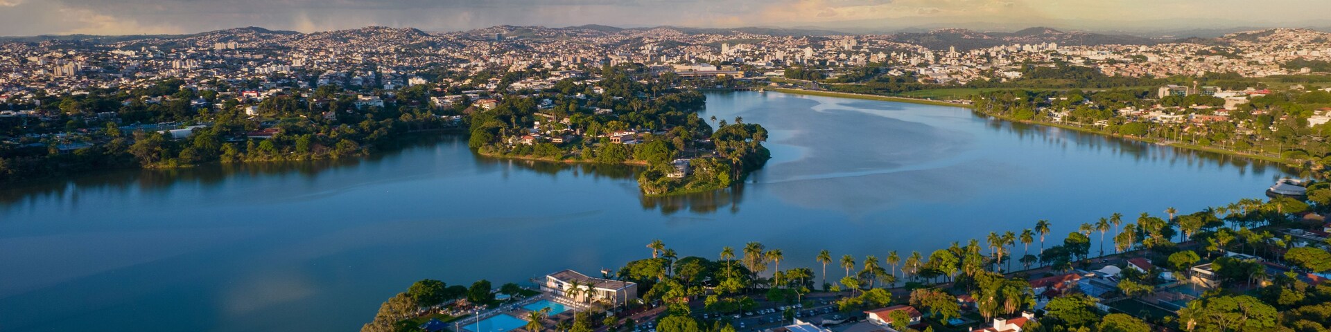 Paisagem costeira urbana com uma grande área de água, região densamente construída e uma pequena ilha com piscina.