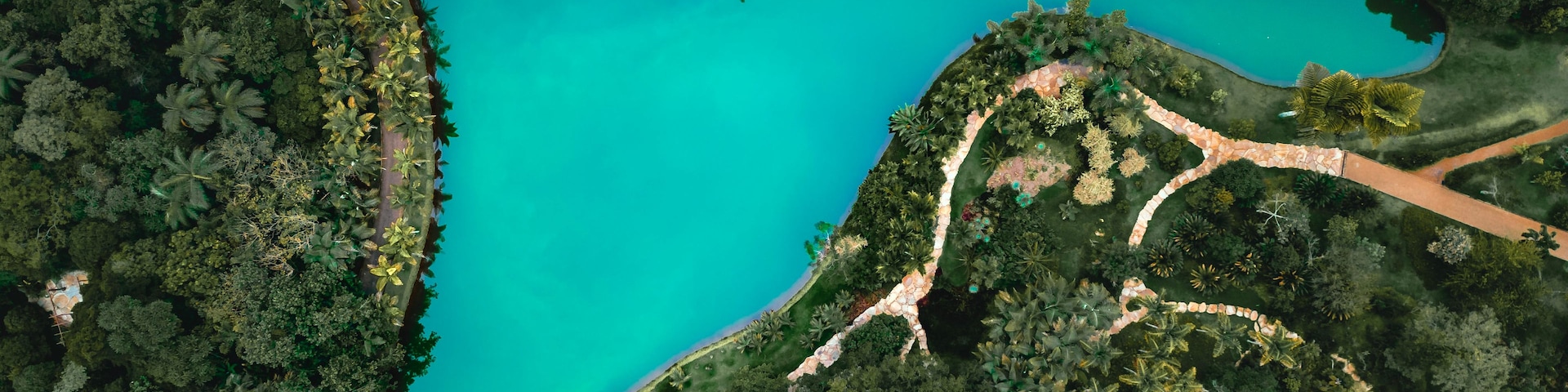 Vista aérea de un parque con un lago turquesa grande, rodeado de abundante vegetación y un sendero sinuoso.