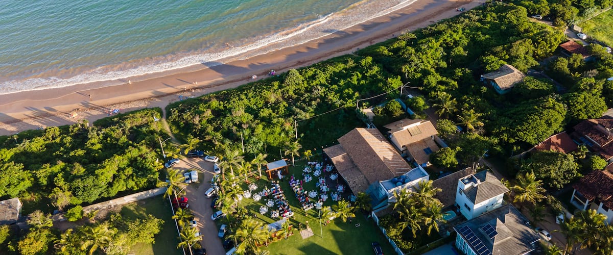 Vista aérea de uma área costeira com praia, vegetação exuberante e edifícios residenciais.