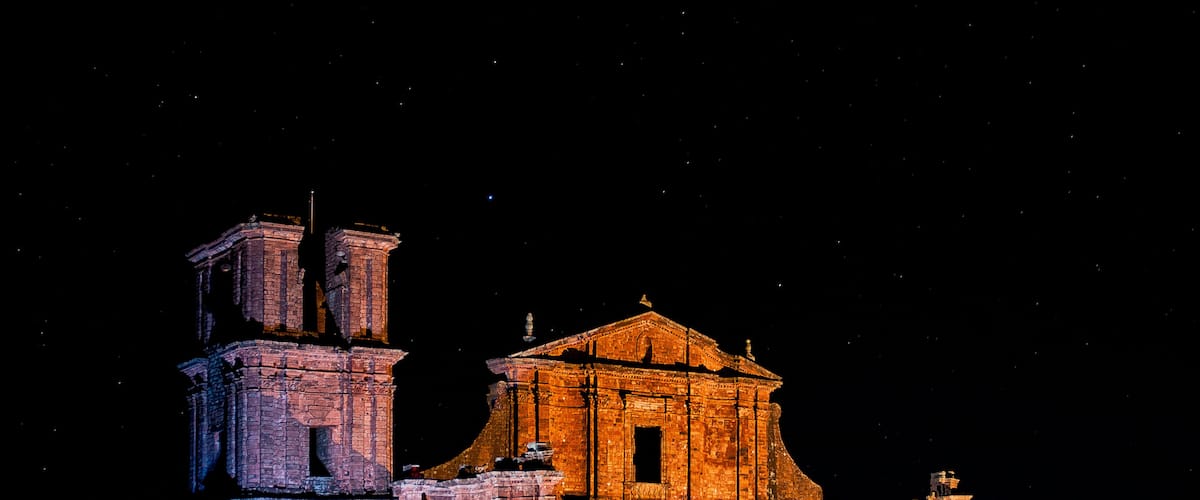 A historic building with a bell tower and a central structure, illuminated at night.