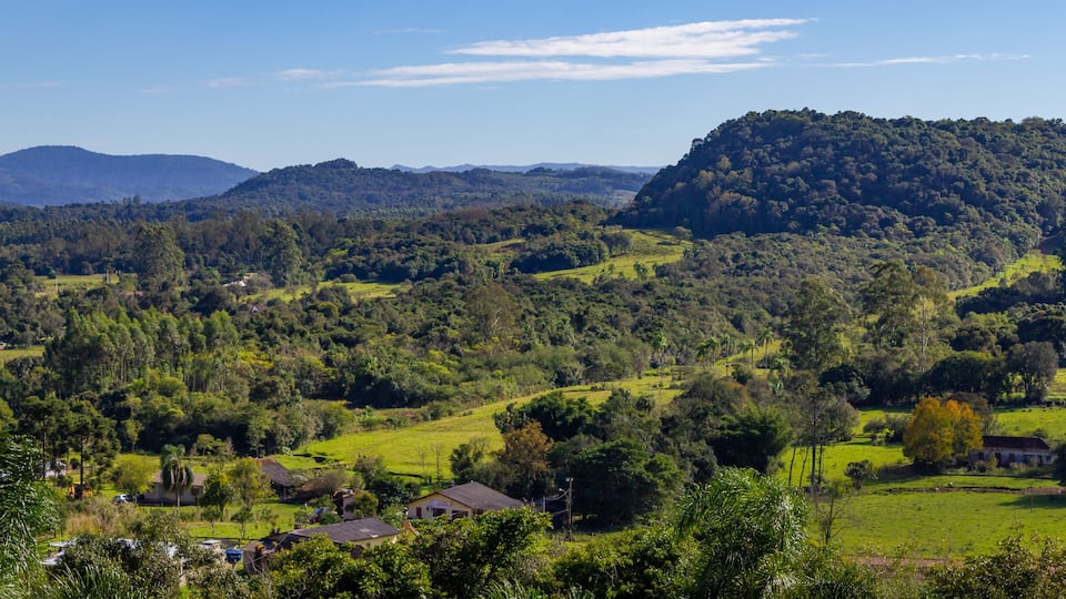 A lush green valley with rolling hills, a small village, and distant mountains under a clear sky.