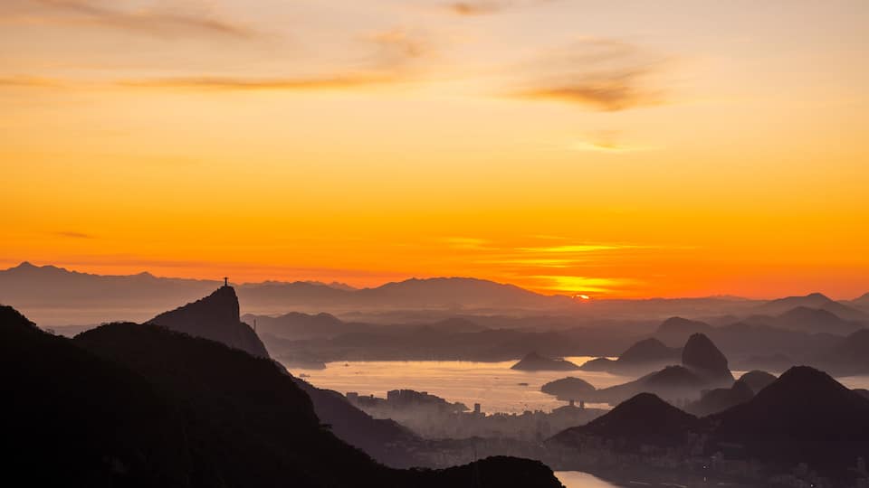 Ein Sonnenuntergang über einer Berglandschaft mit einem markanten Gipfel und einer Stadt im Tal.