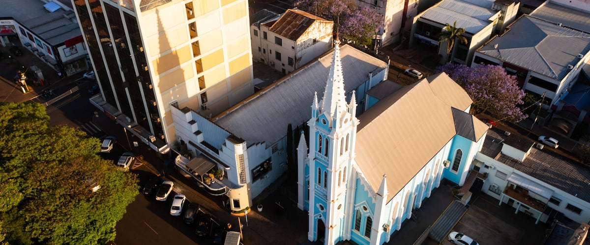 An aerial view of a cityscape with a prominent church featuring a blue facade and a tall spire, surrounded by modern buildings and parked cars.