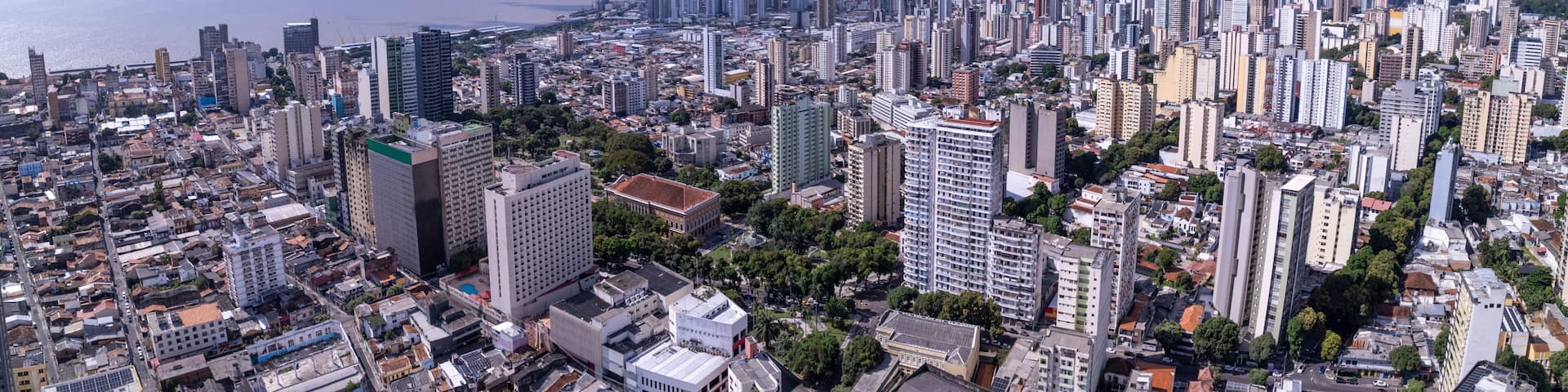 A densely populated cityscape with numerous high-rise buildings, a large body of water in the distance, and a clear sky.