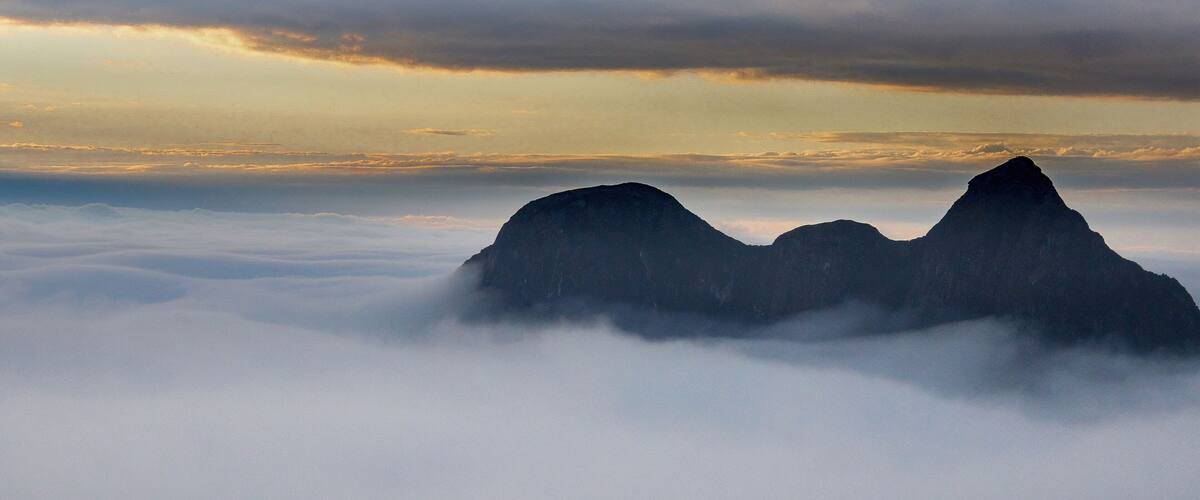 A mountain range above a sea of clouds with a cloudy sky.
