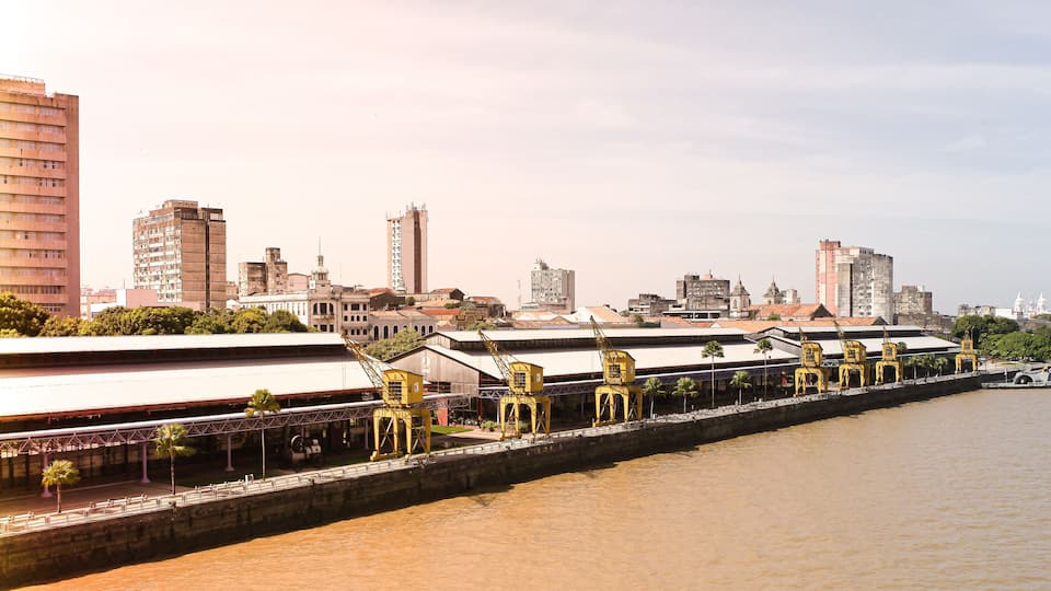 A riverside cityscape with a prominent bridge, high-rise buildings, and a waterfront promenade.