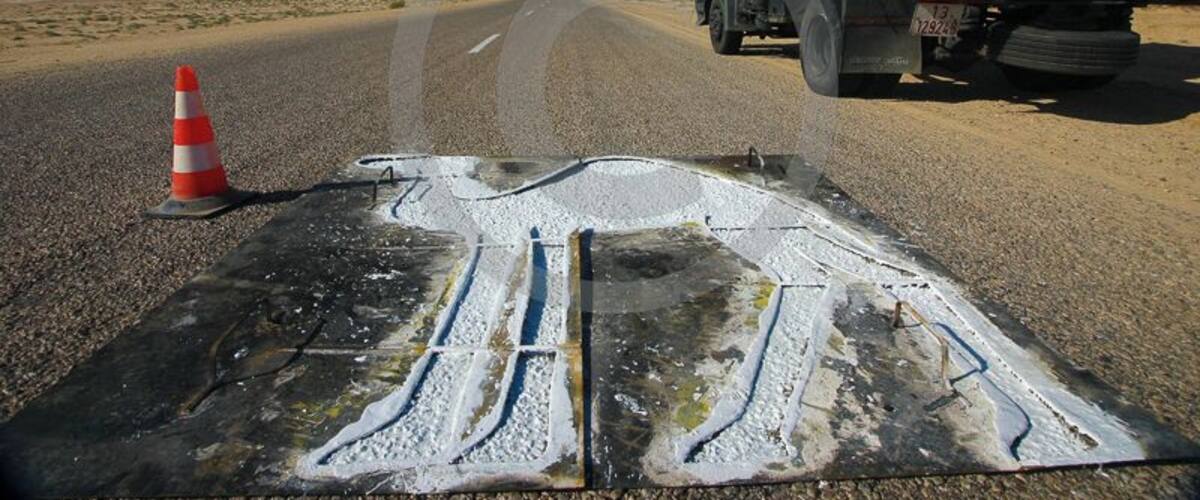 A road with a white road marking, a traffic cone, and a yellow truck.