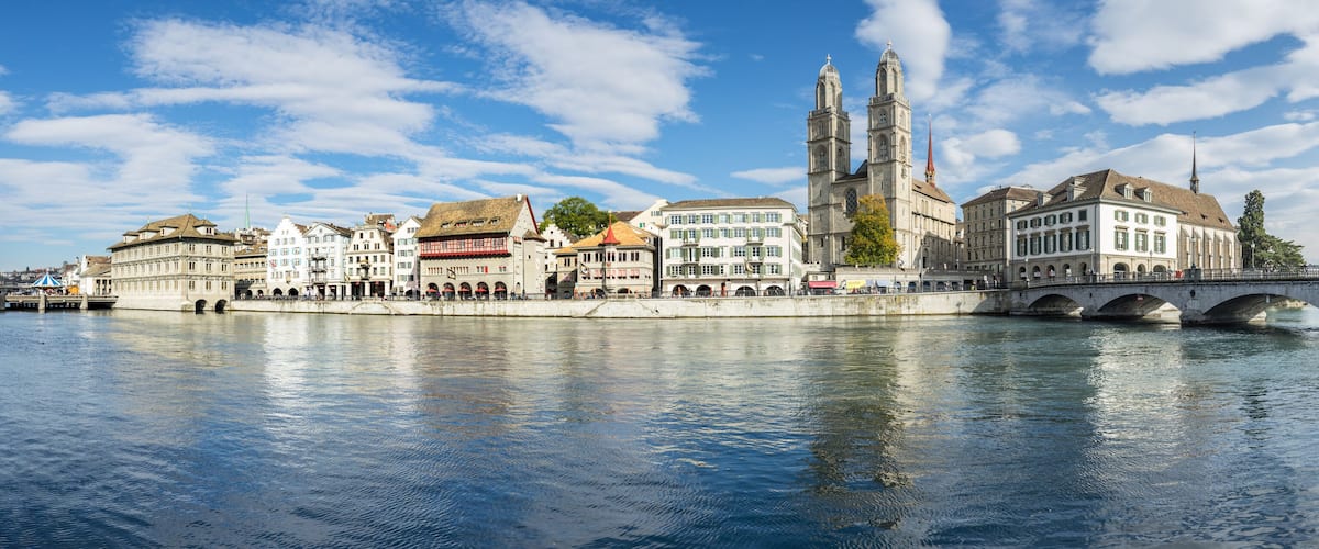 A river with a stone bridge, historic buildings, and a prominent church with twin towers.