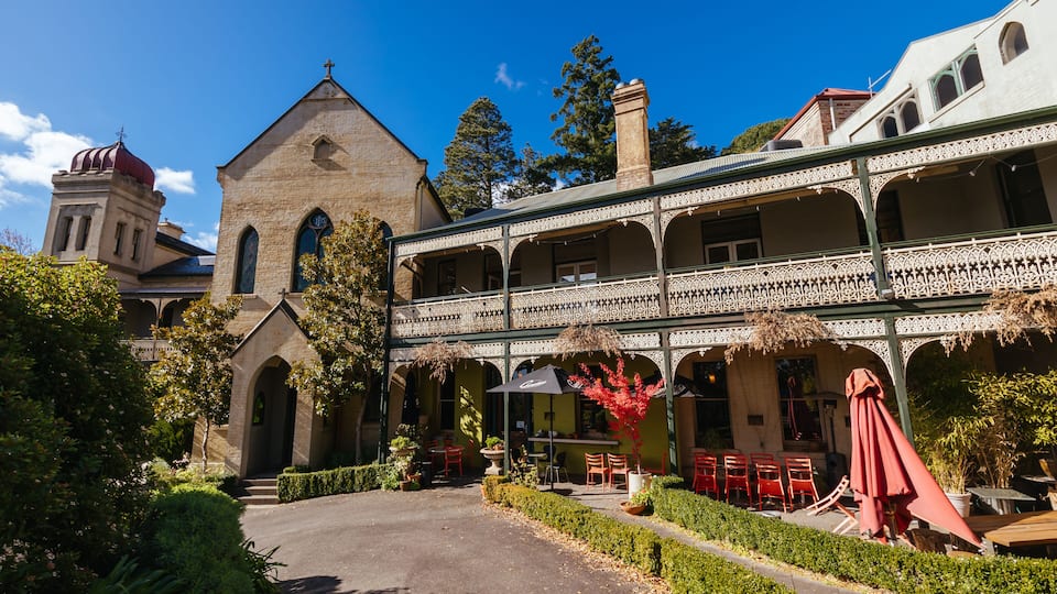 A historic building with a prominent tower and arched windows, surrounded by well-maintained gardens and outdoor seating.