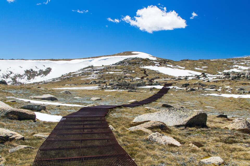 A snowy mountain landscape with a rocky path and a clear blue sky.