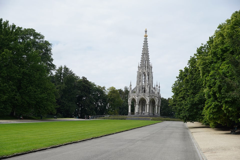 A grand Gothic-style cathedral with intricate spires and a tall tower, surrounded by lush green trees and a well-maintained lawn.