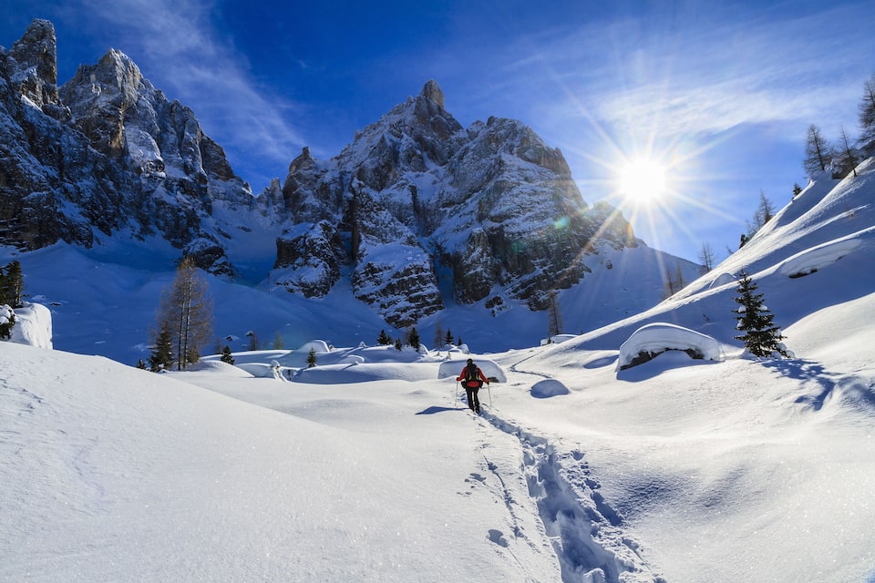 A snowy mountain landscape with a climber in red, snow-covered peaks, and a clear blue sky.