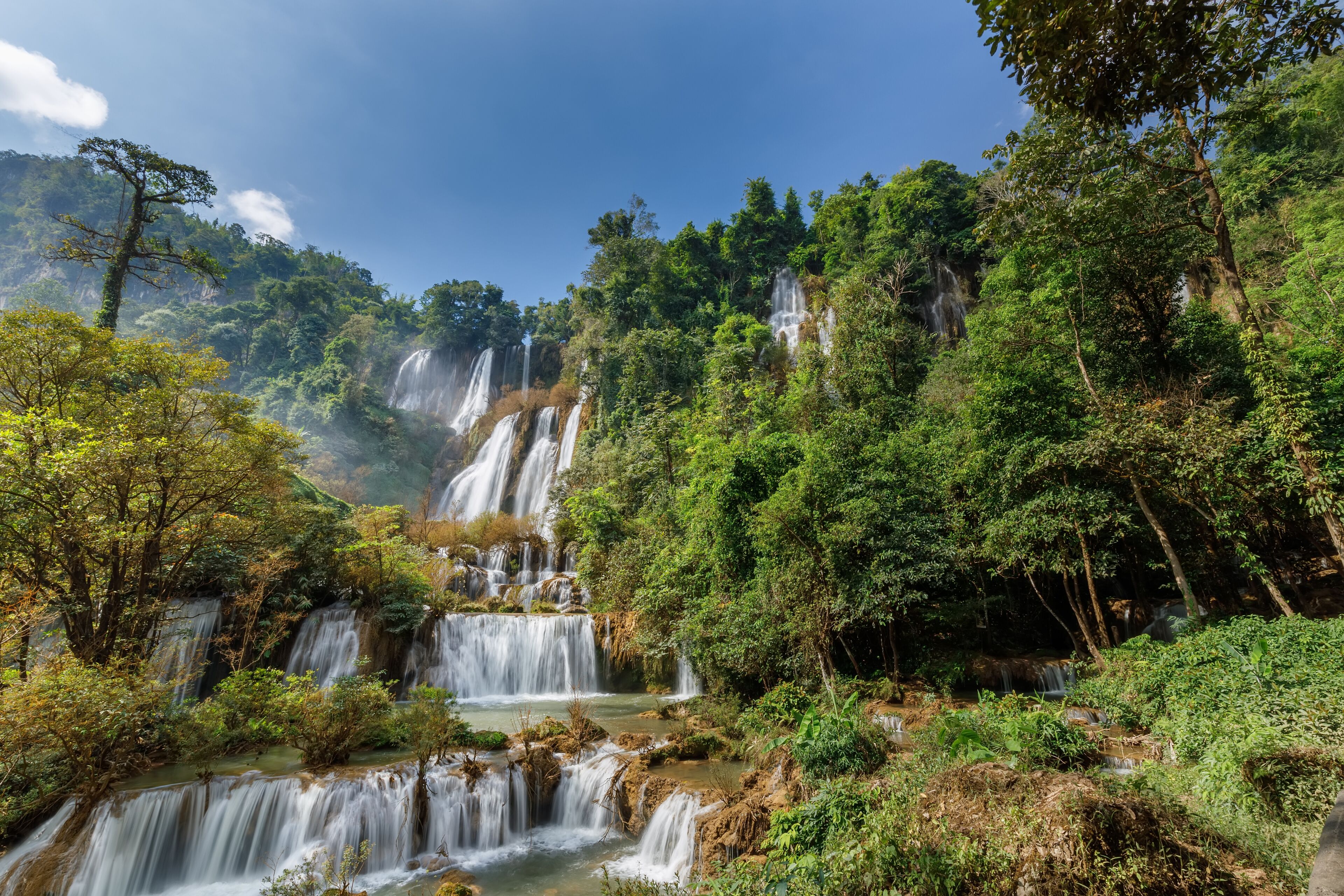 A multi-tiered waterfall surrounded by dense forest.