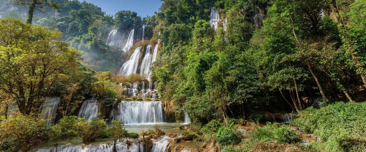 A multi-tiered waterfall surrounded by dense forest.