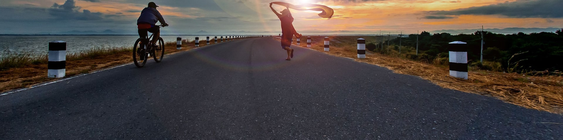 Une route où l’on voit des cyclistes, un coucher de soleil et une étendue d’eau.