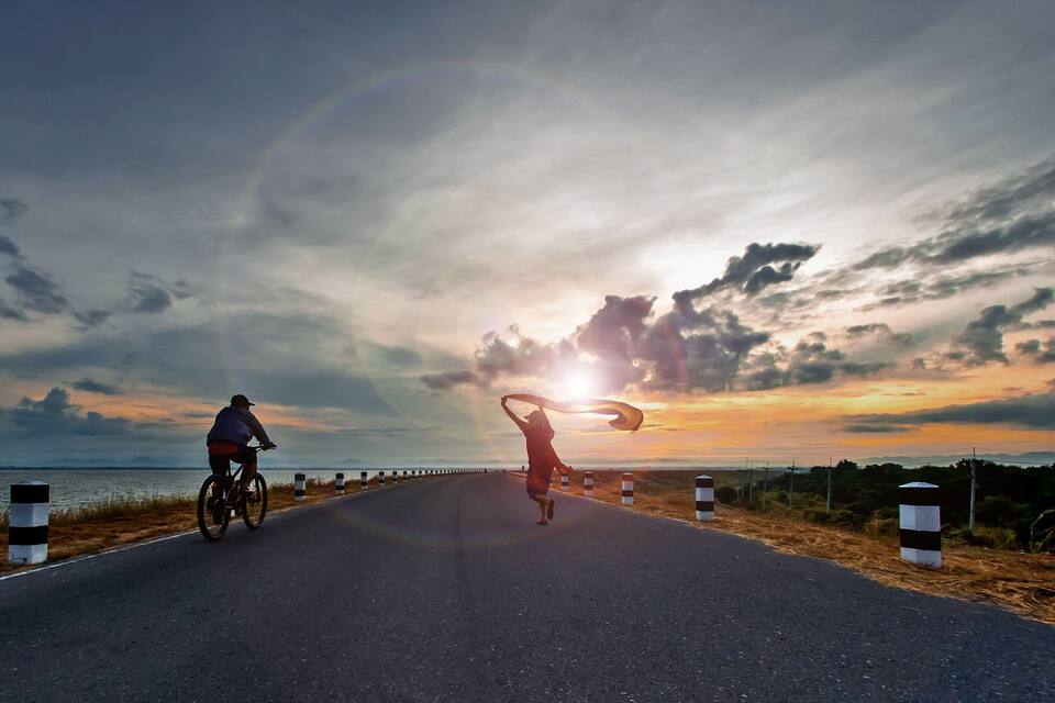 A road with cyclists, a sunset, and a body of water.