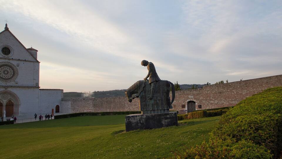 A statue of a knight on horseback in front of a historic building with a clock tower.