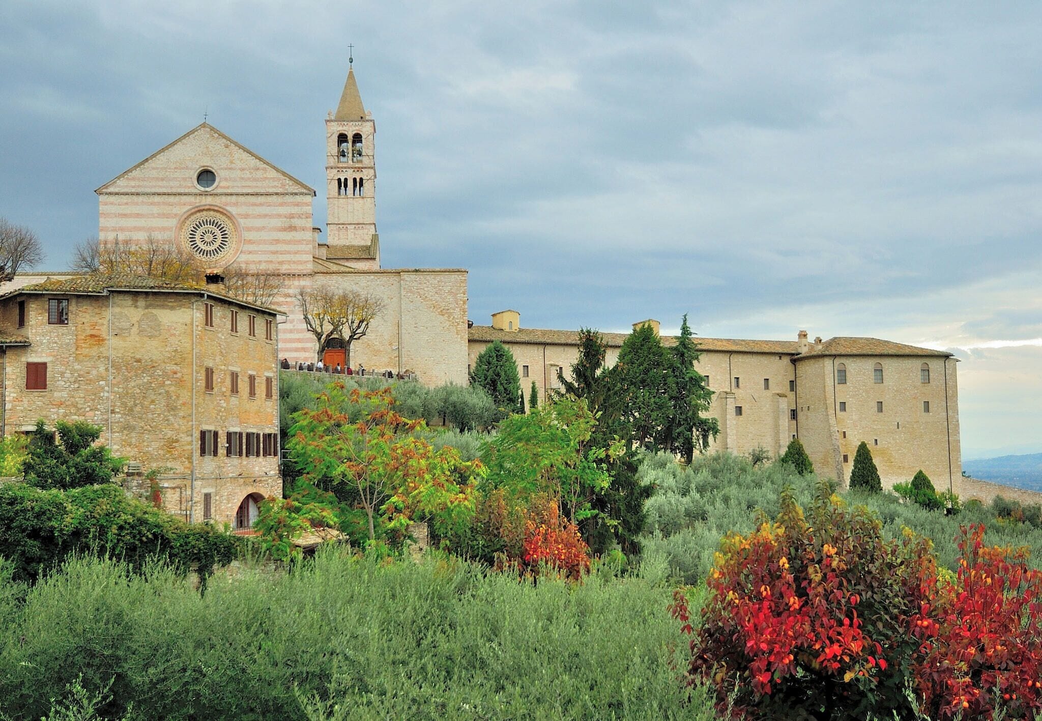A historic building with a bell tower and a clock, surrounded by lush greenery and autumn-colored trees.