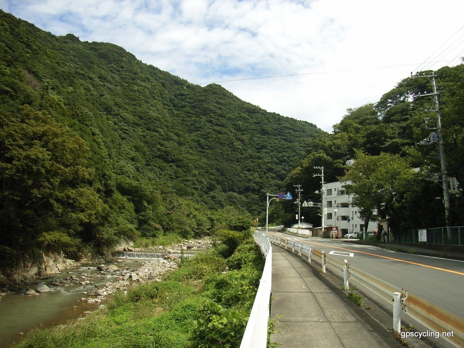 Um rio serpenteando por uma região montanhosa, com uma ponte e uma estrada ao lado.