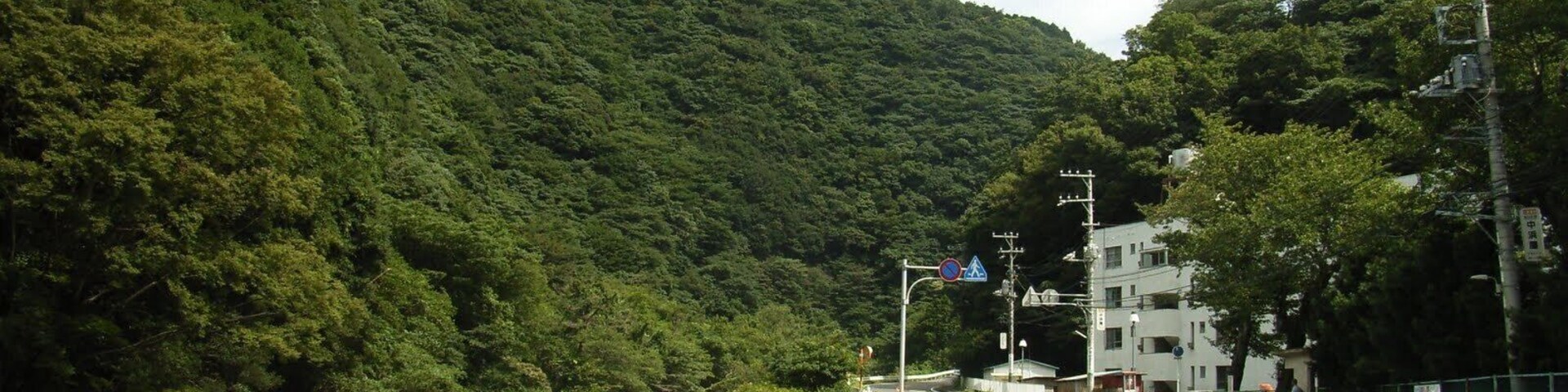 Um rio serpenteando por uma região montanhosa, com uma ponte e uma estrada ao lado.