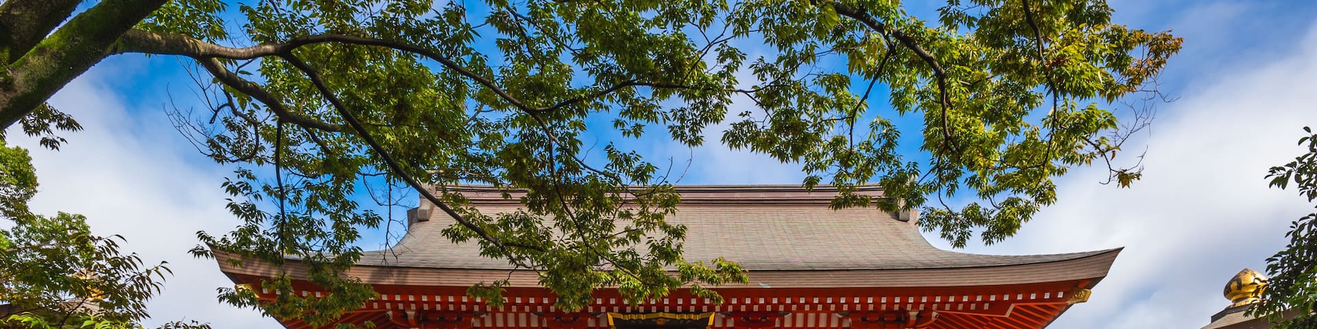 A traditional Japanese temple with a red and white facade, green trees, and a clear blue sky.