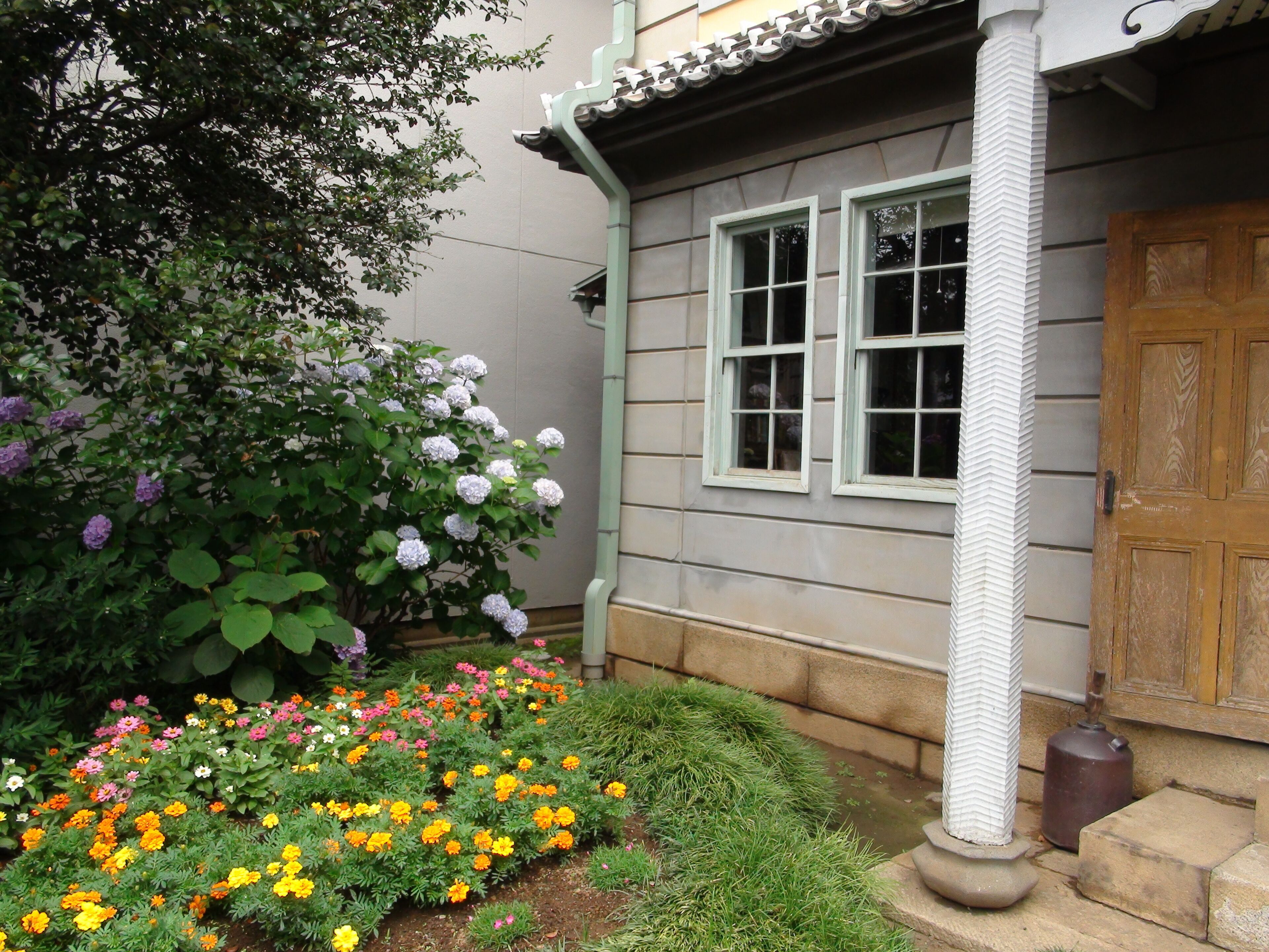 A house with a garden featuring marigolds, hydrangeas, and other flowers.