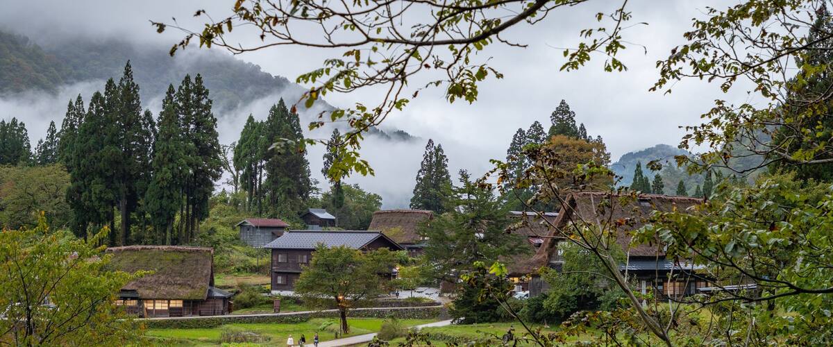 A traditional village with thatched-roof houses, terraced fields, and a misty mountain backdrop.