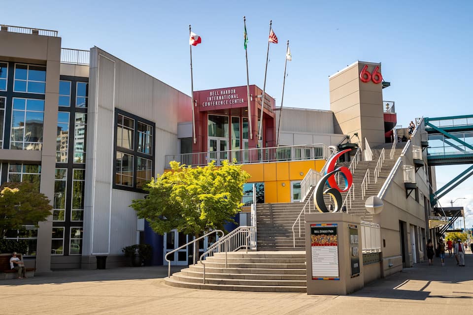 Centro de Convenções Internacionais Bell Harbor com um grande letreiro '66', bandeiras e uma escadaria que leva à entrada.