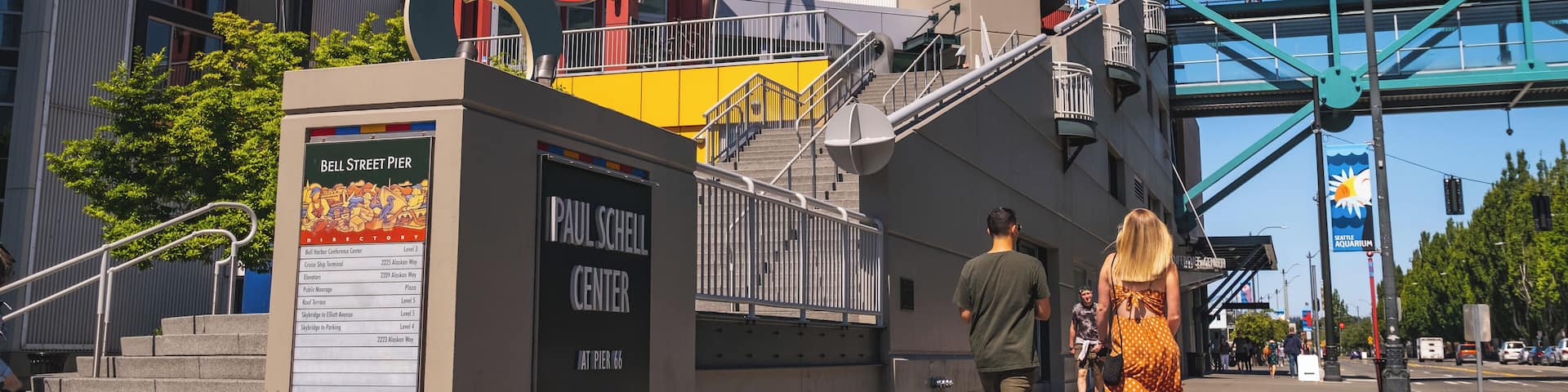 A modern building with a large sign for the Paul Schell Center, a staircase, and a pedestrian bridge.