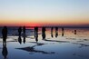 Silhouetten van mensen die staan op een nat, reflecterend oppervlak tijdens de zonsondergang.
