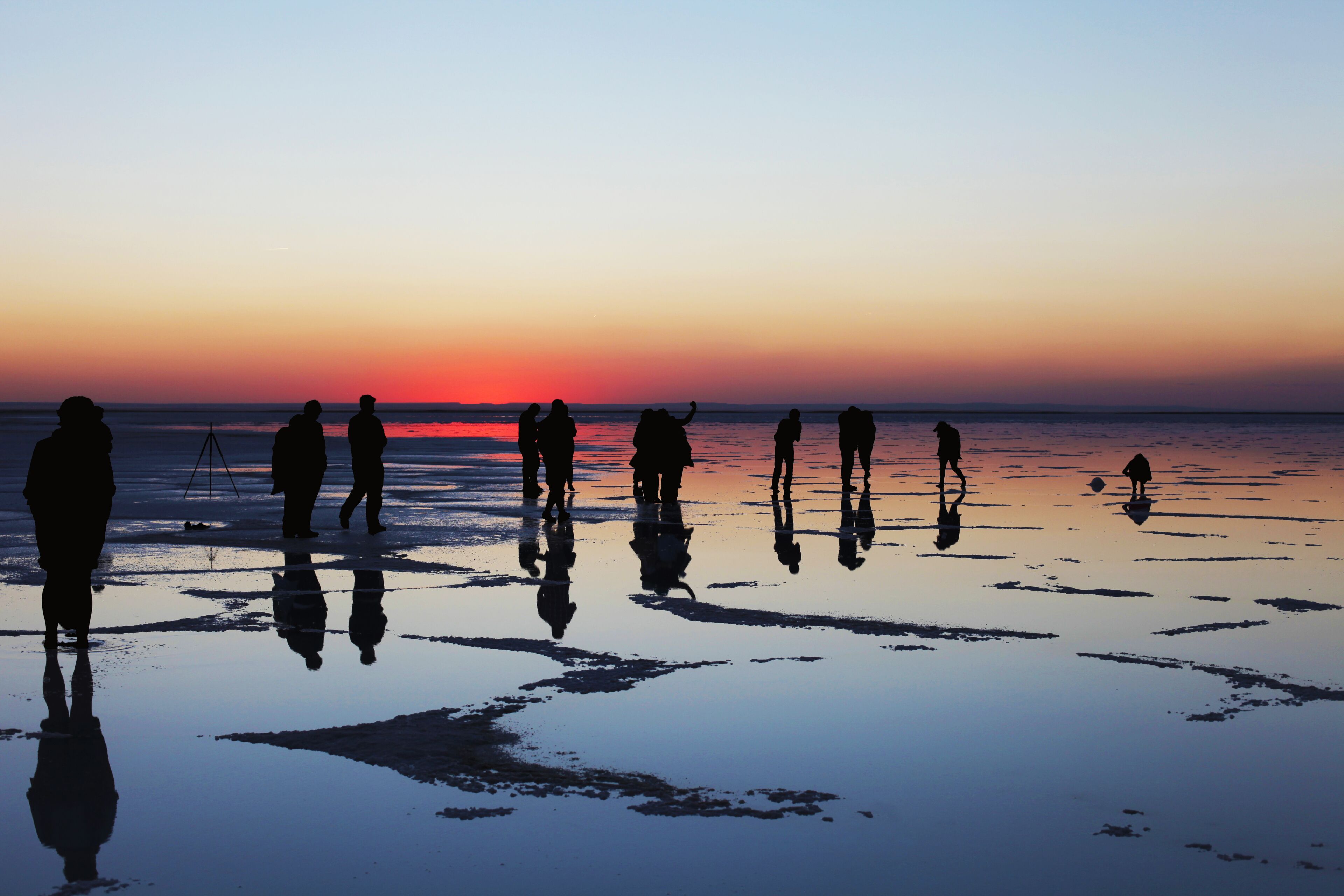 Silhouettes of people standing on a reflective wet surface at sunset.