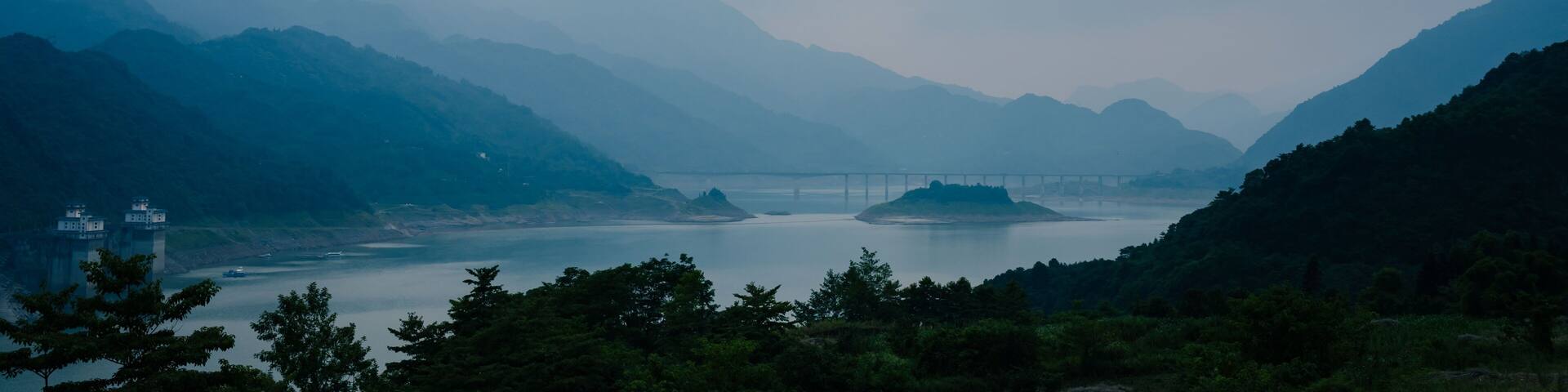 Un paisaje montañoso con un puente sobre un río tranquilo.