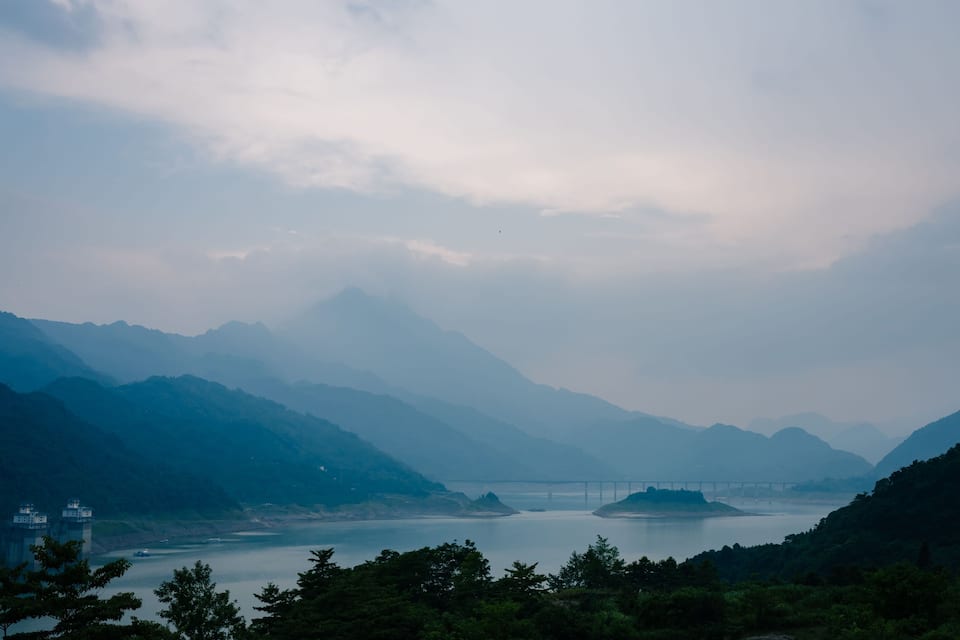 A mountainous landscape with a bridge over a calm river.