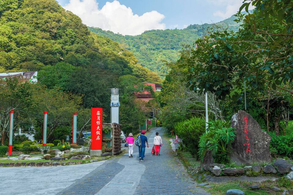 A pathway leading uphill with a signpost, a large rock with red text, and lush greenery.