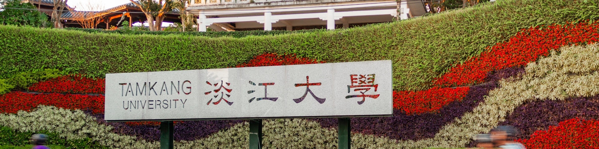Placa da Universidade Tamkang com um jardim florido colorido ao fundo.