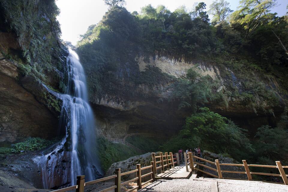 Ein Wasserfall stürzt über eine felsige Klippe, umgeben von üppiger Vegetation.