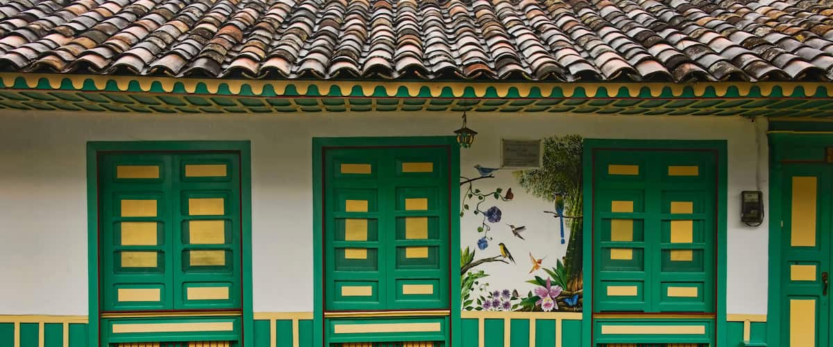 A building with green and yellow doors, a tiled roof, and a mural of birds and flowers.