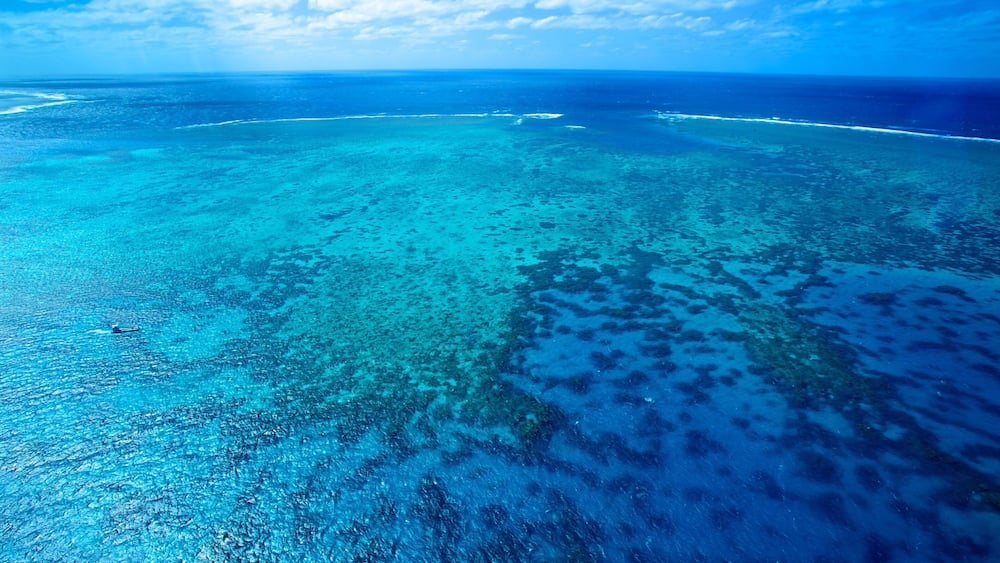 A turquoise sea with coral reefs and a small boat.