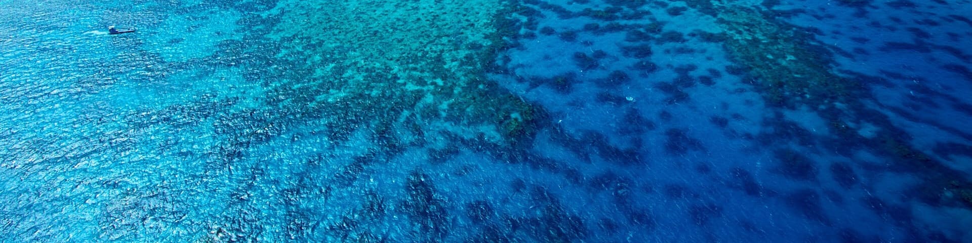 A turquoise sea with coral reefs and a small boat.