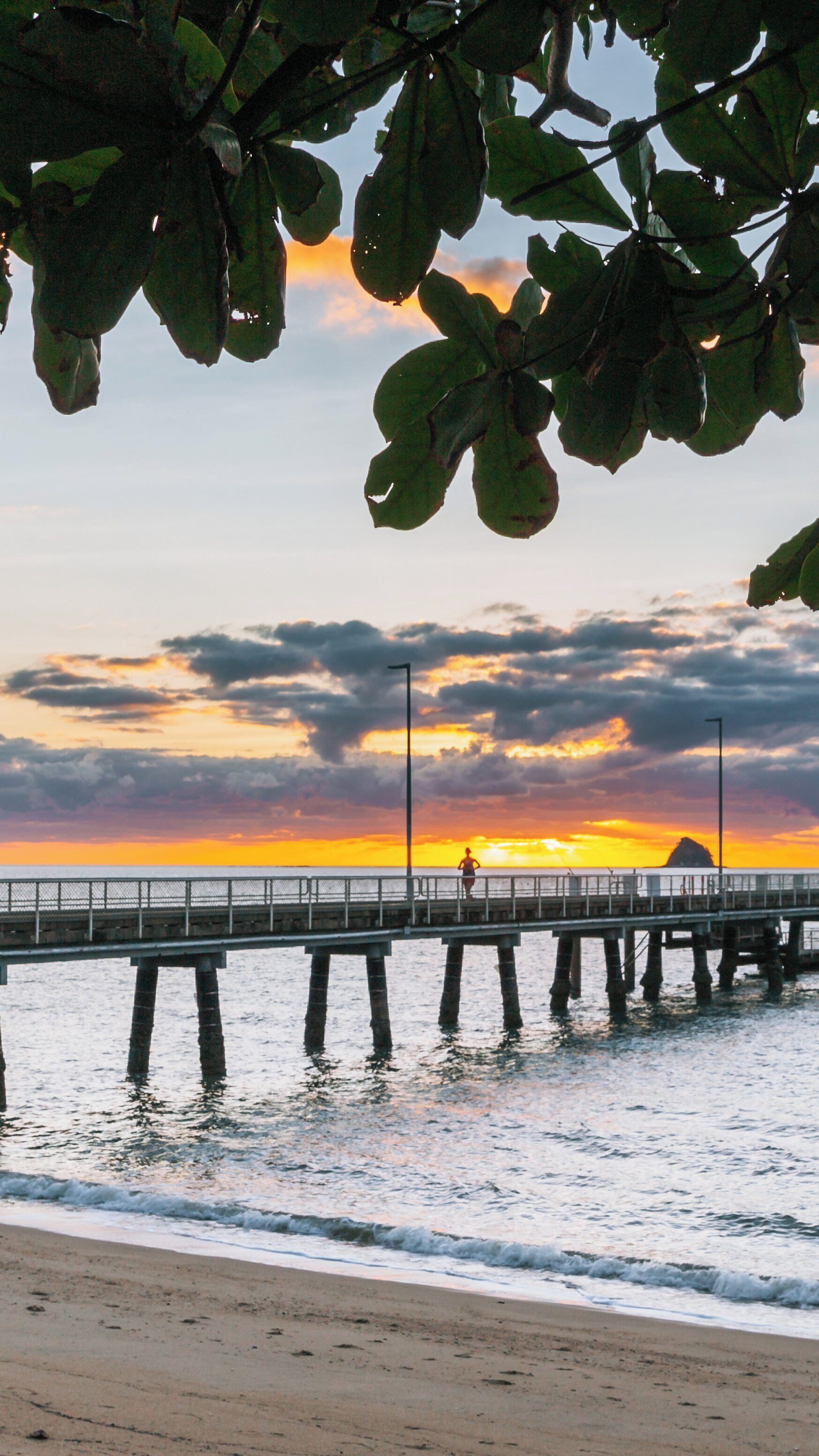 Sunset casting vibrant hues over Palm Cove Beach with pier and calm waters in Cairns, Queensland, Australia