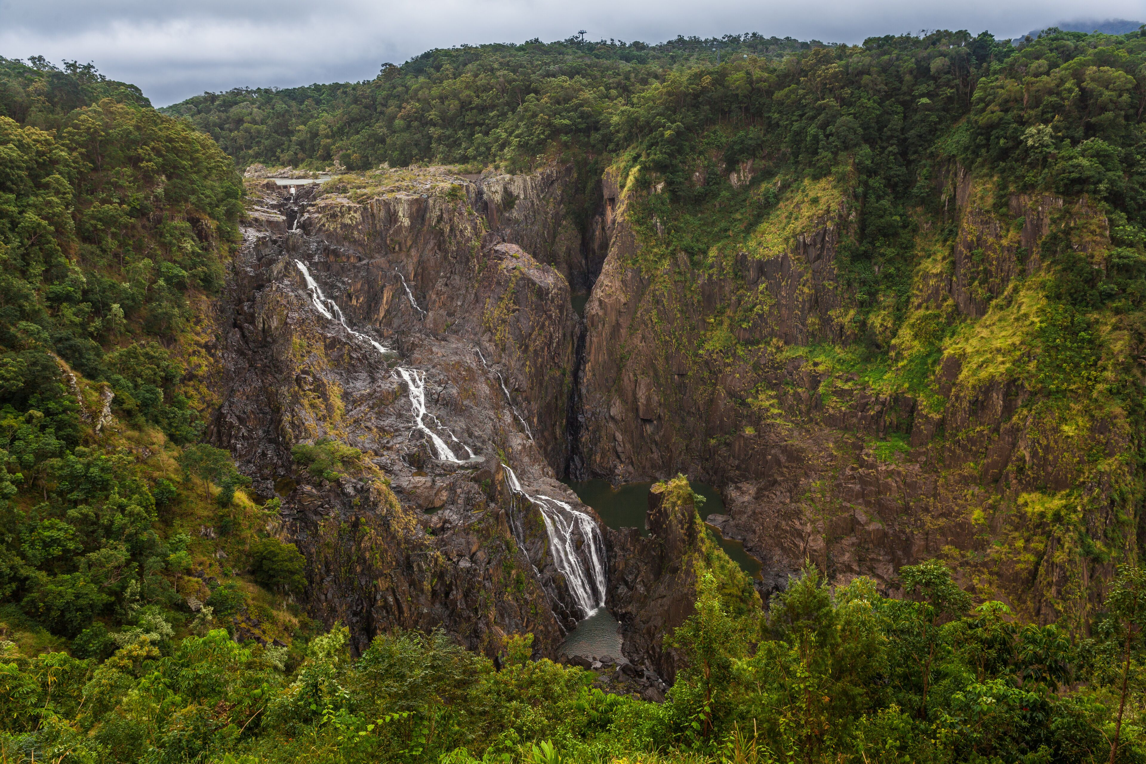 A multi-tiered waterfall cascading down a steep, rocky cliff surrounded by dense, green forest.