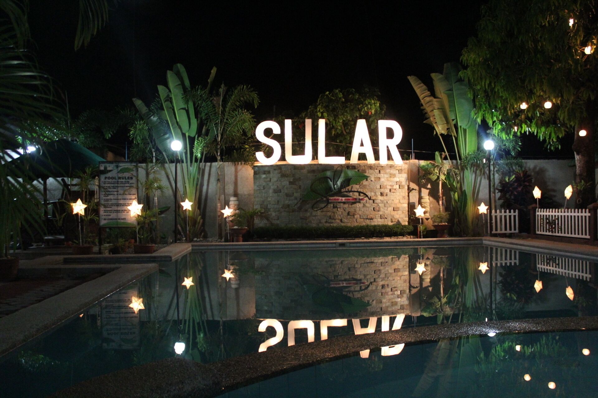 A pool area with a sign that reads "SULAR" and a wall with a plant mural.