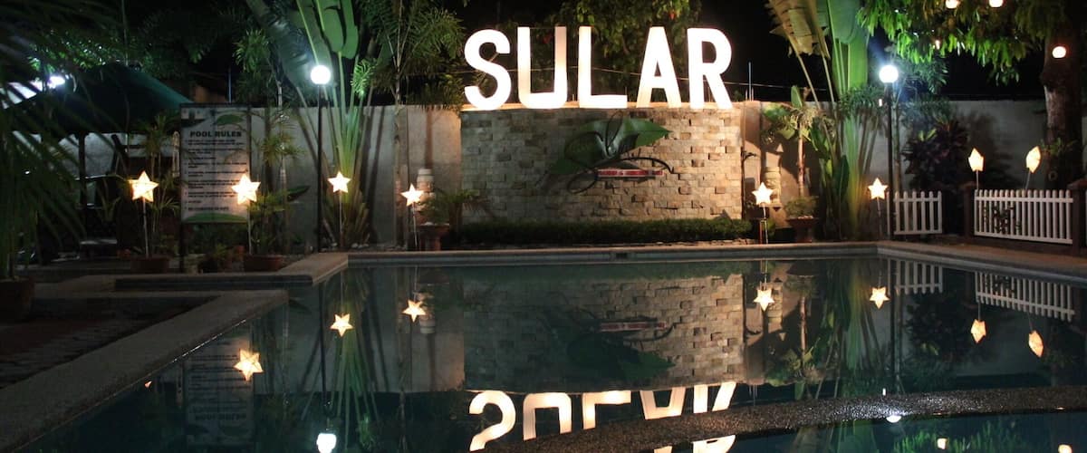 A pool area with a sign that reads "SULAR" and a wall with a plant mural.