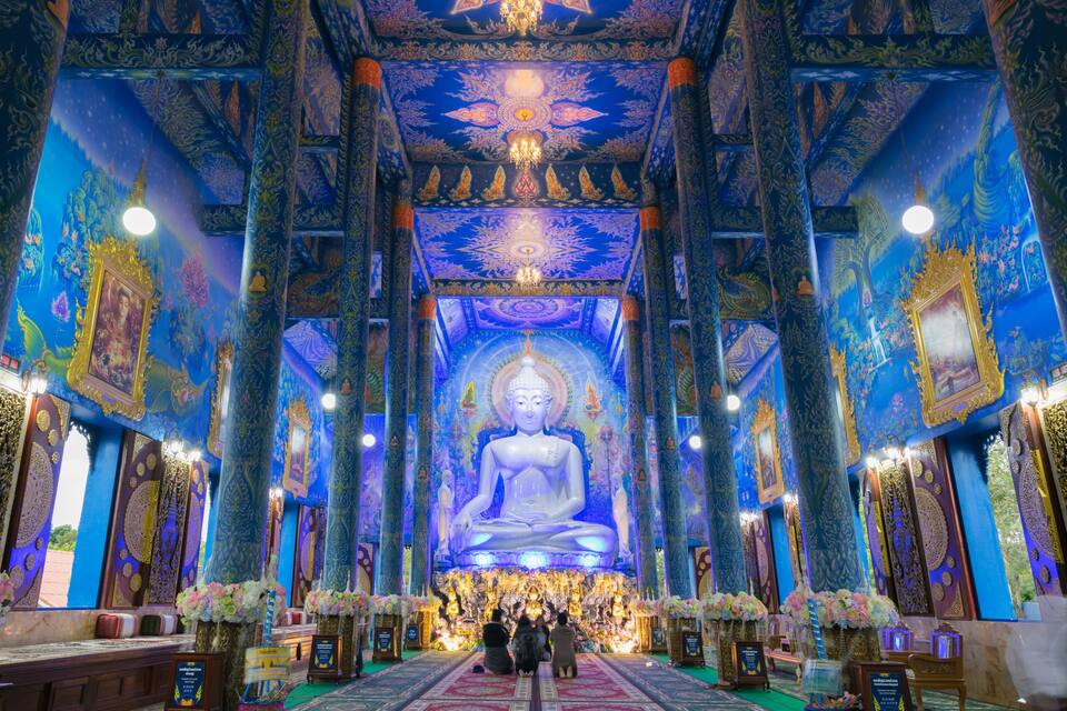 Una gran estàtua de Buda en un temple amb decoracions intricades daurades i blaves.