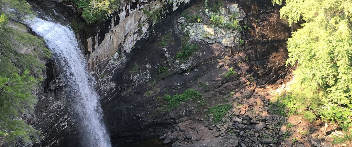 A waterfall cascading into a river surrounded by rocky cliffs and greenery.