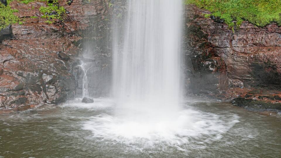 A waterfall cascading down a rocky cliff surrounded by greenery.