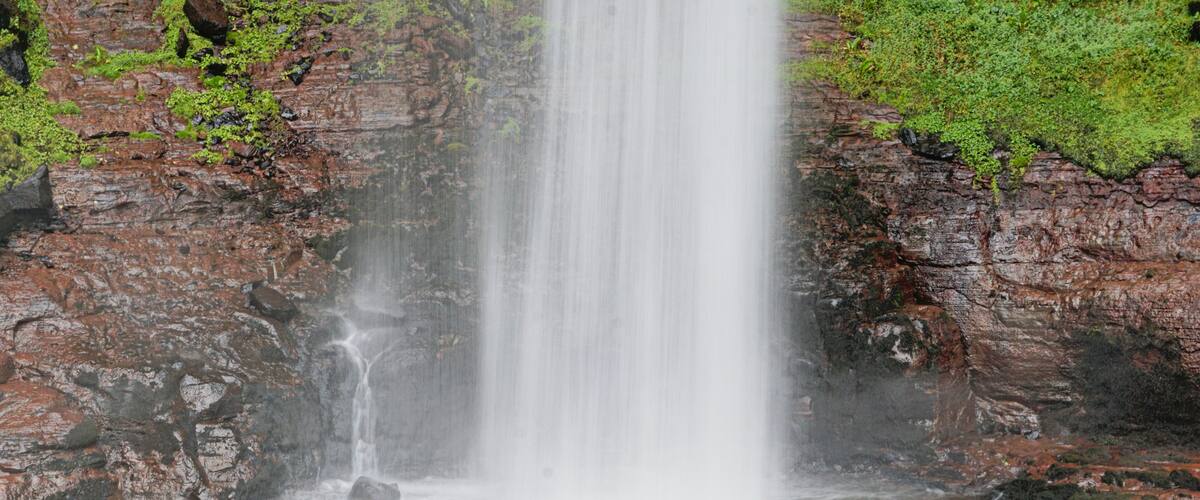 A waterfall cascading down a rocky cliff surrounded by greenery.